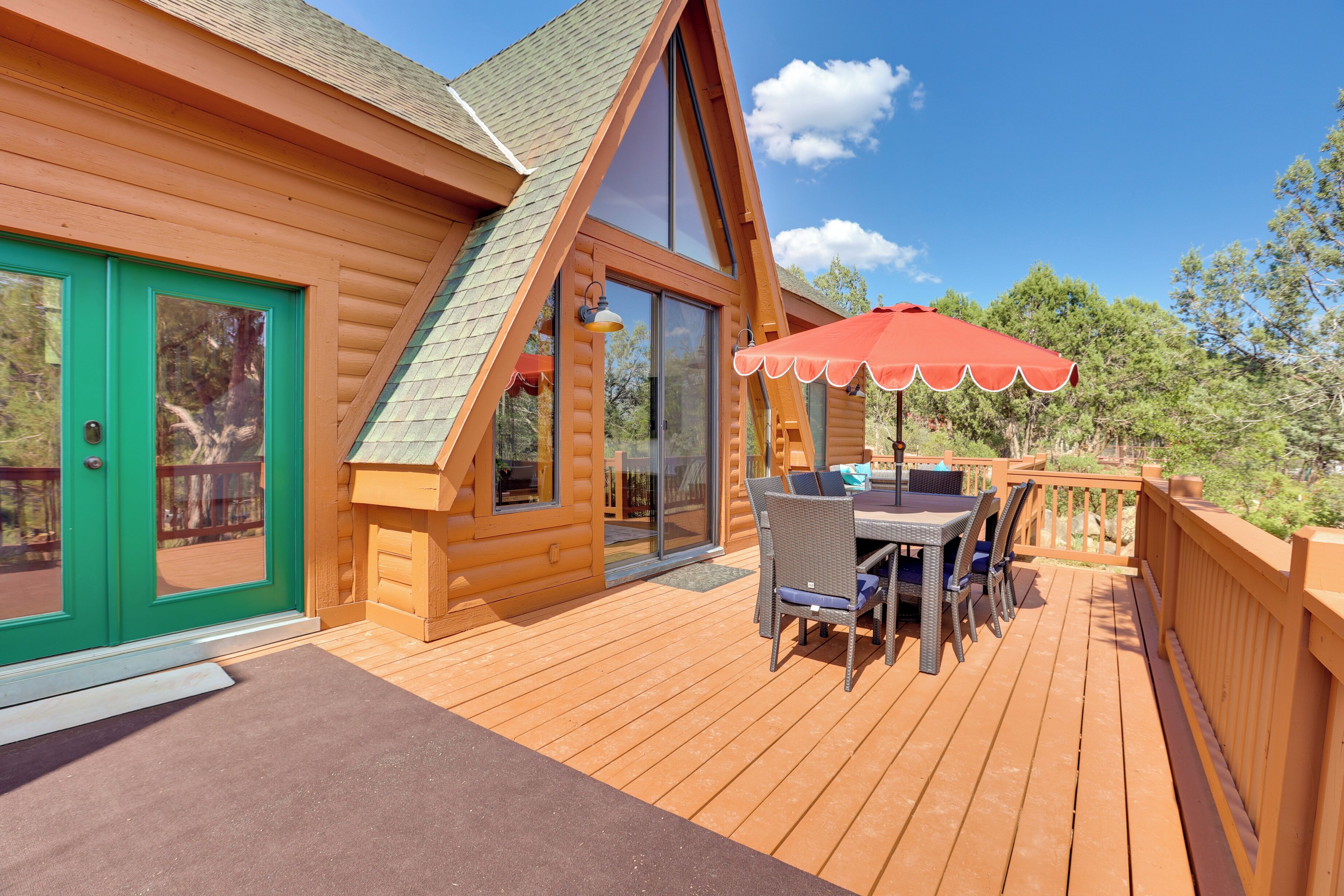 A wooden cabin with a deck, a dining area with outdoor furniture, and a red umbrella.