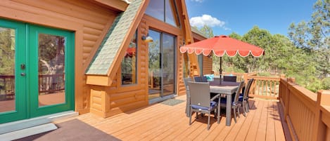 A wooden cabin with a deck, a dining area with outdoor furniture, and a red umbrella.
