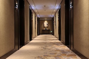 Un couloir d’hôtel avec un sol recouvert de moquette, un tableau accroché au mur et un comptoir de réception au bout.