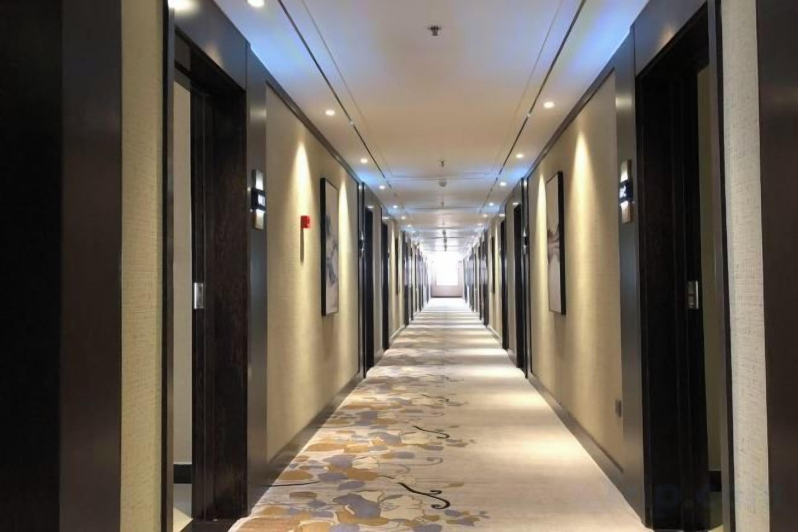Un pasillo de hotel con puertas a ambos lados, alfombra estampada e iluminación en el techo.