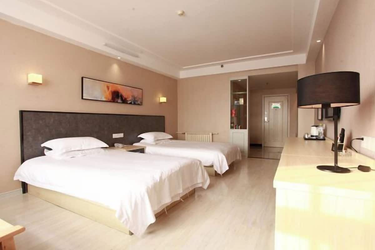 A hotel room with two beds, a bedside table, a lamp, and a painting on the wall.