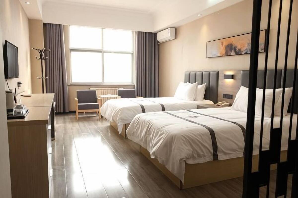 A hotel room with two beds, a desk, a chair, a TV, and a window with curtains.