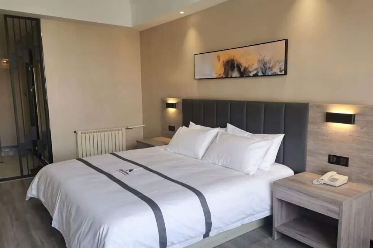 A hotel room with a large bed, bedside lamps, a nightstand, and a framed picture on the wall.