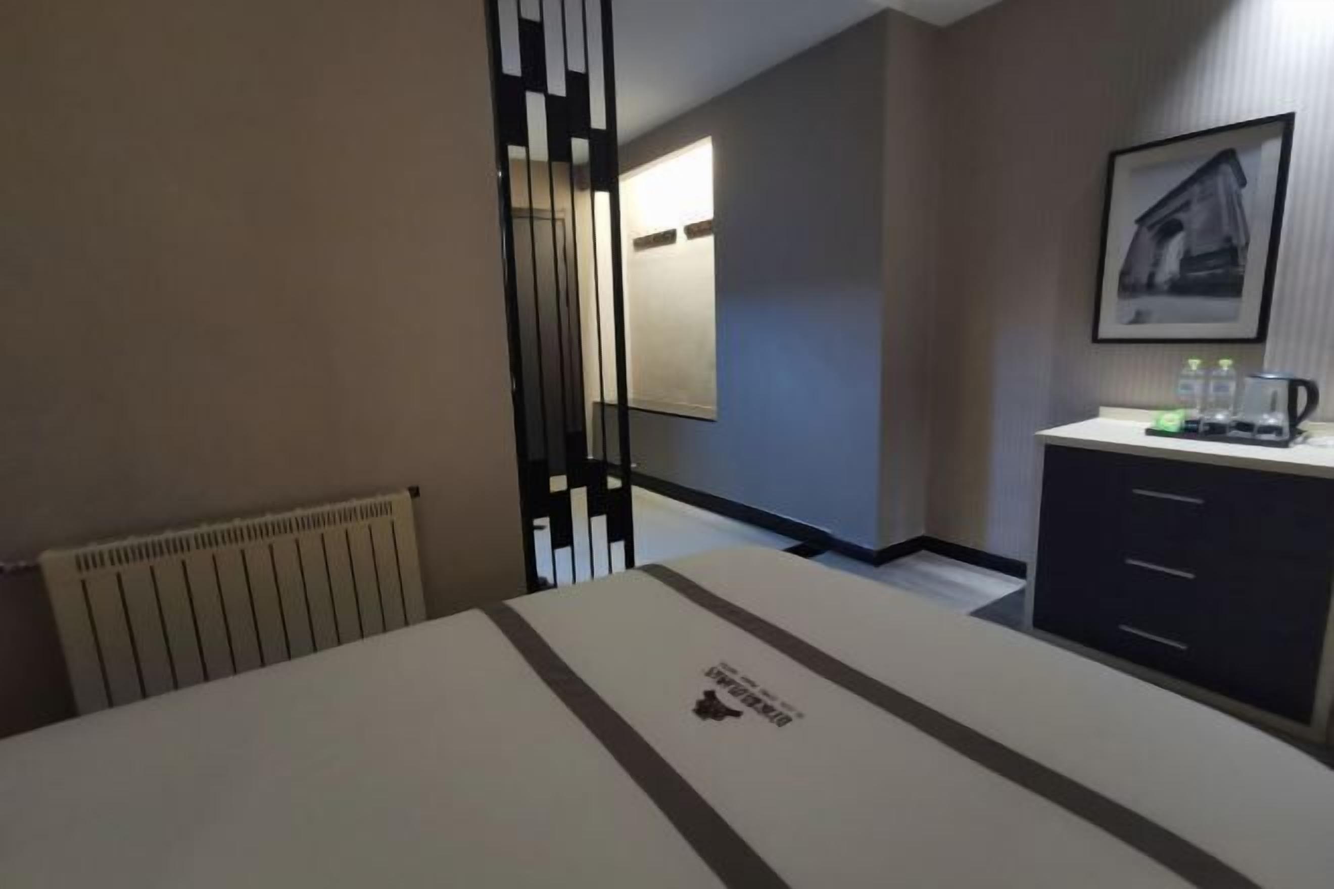 A hotel room with a bed, a radiator, a mirror, a sink, and a framed picture on the wall.