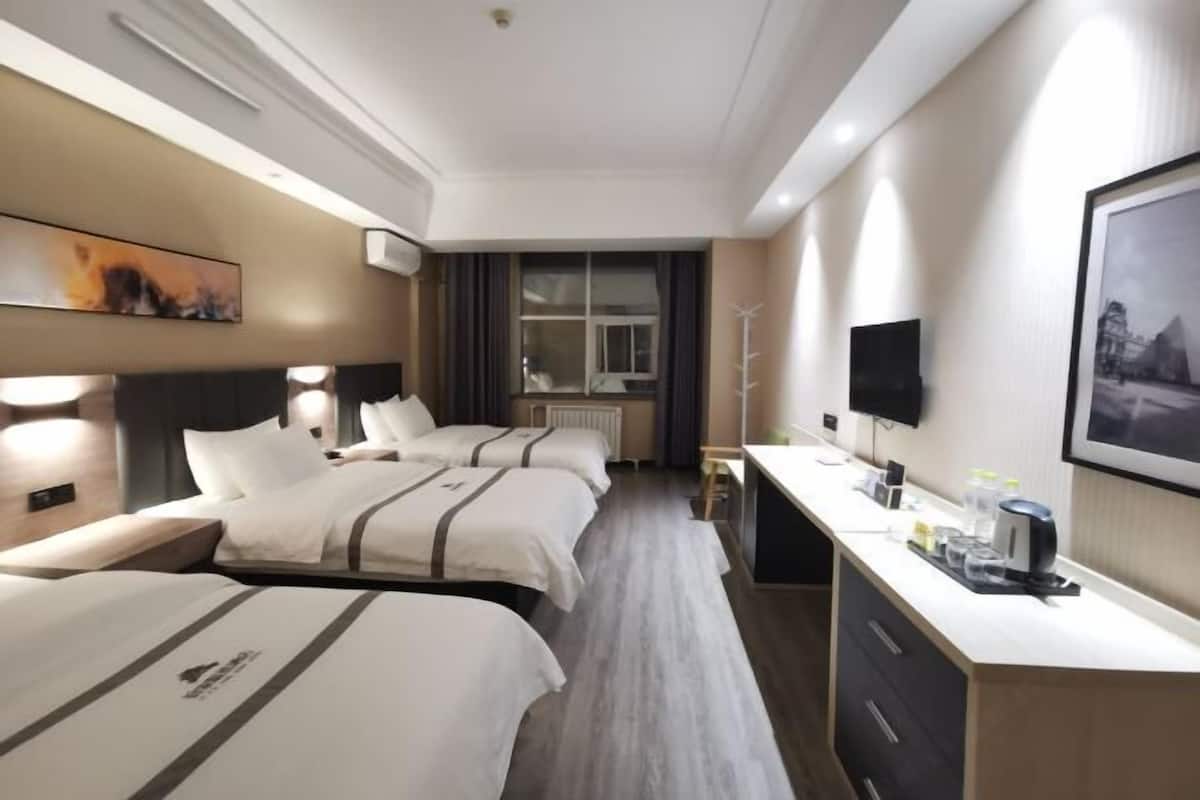 A hotel room with two beds, a desk, a flat-screen TV, and a window with curtains.