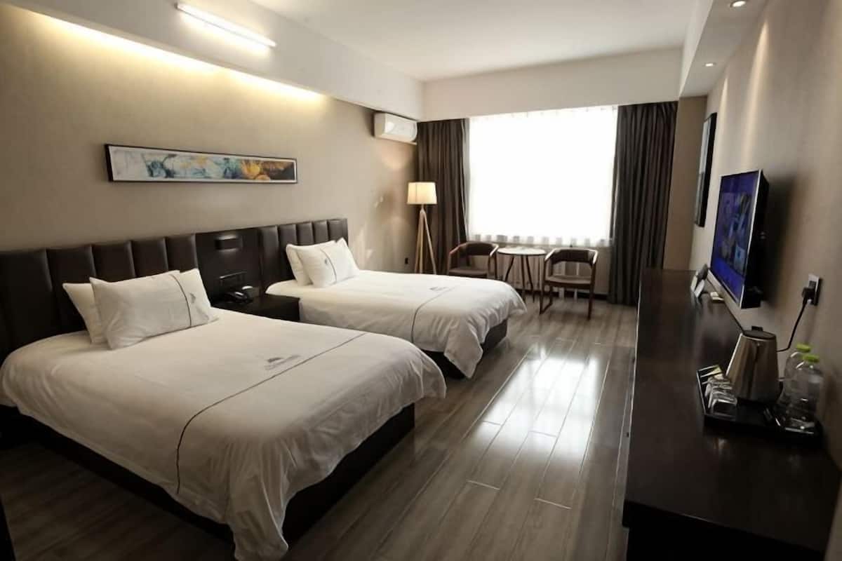 A hotel room with two beds, a desk, a chair, a TV, and a window with curtains.