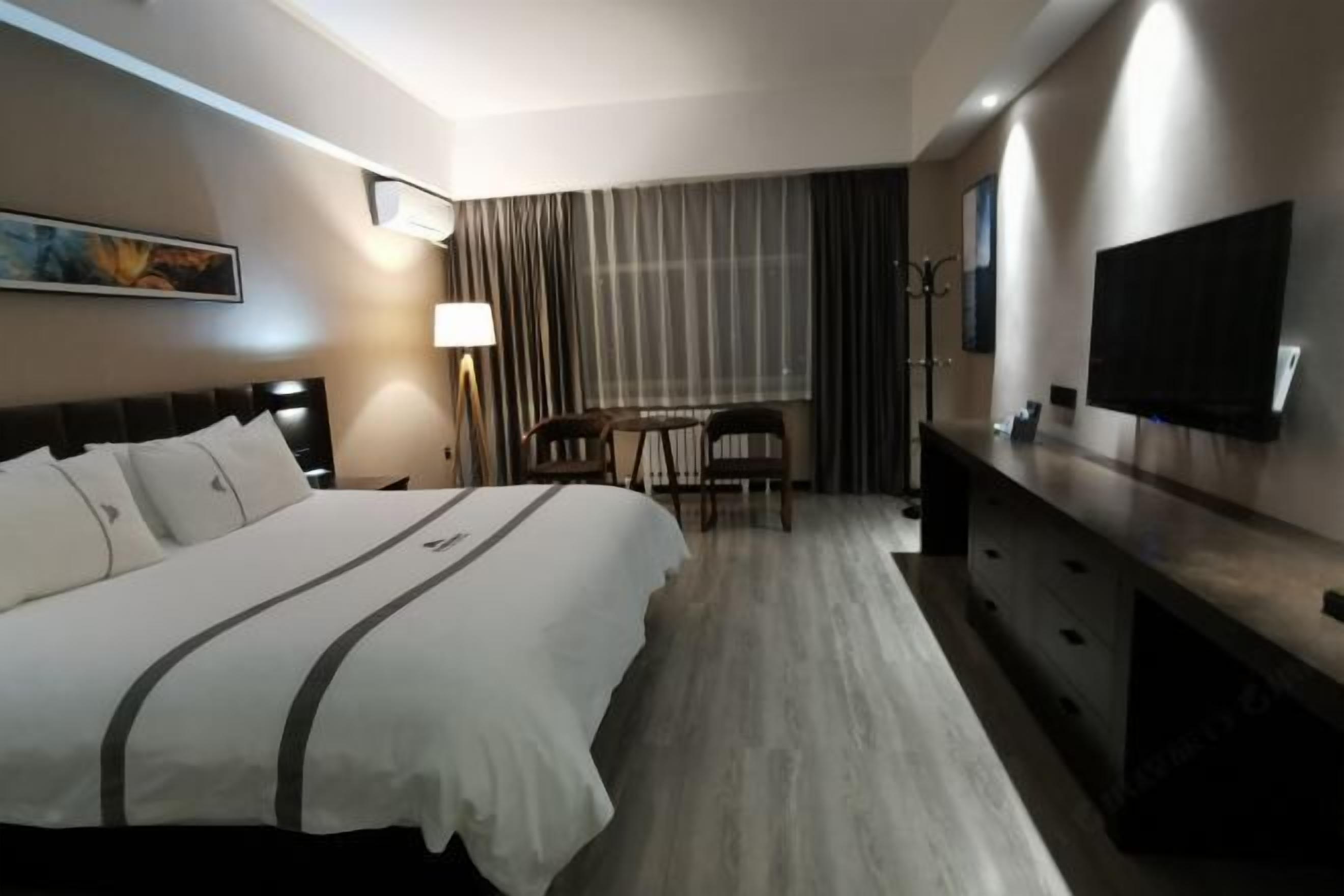 A hotel room with a large bed, a desk, a TV, and a lamp.