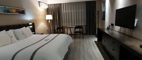 A hotel room with a large bed, a desk, a TV, and a lamp.