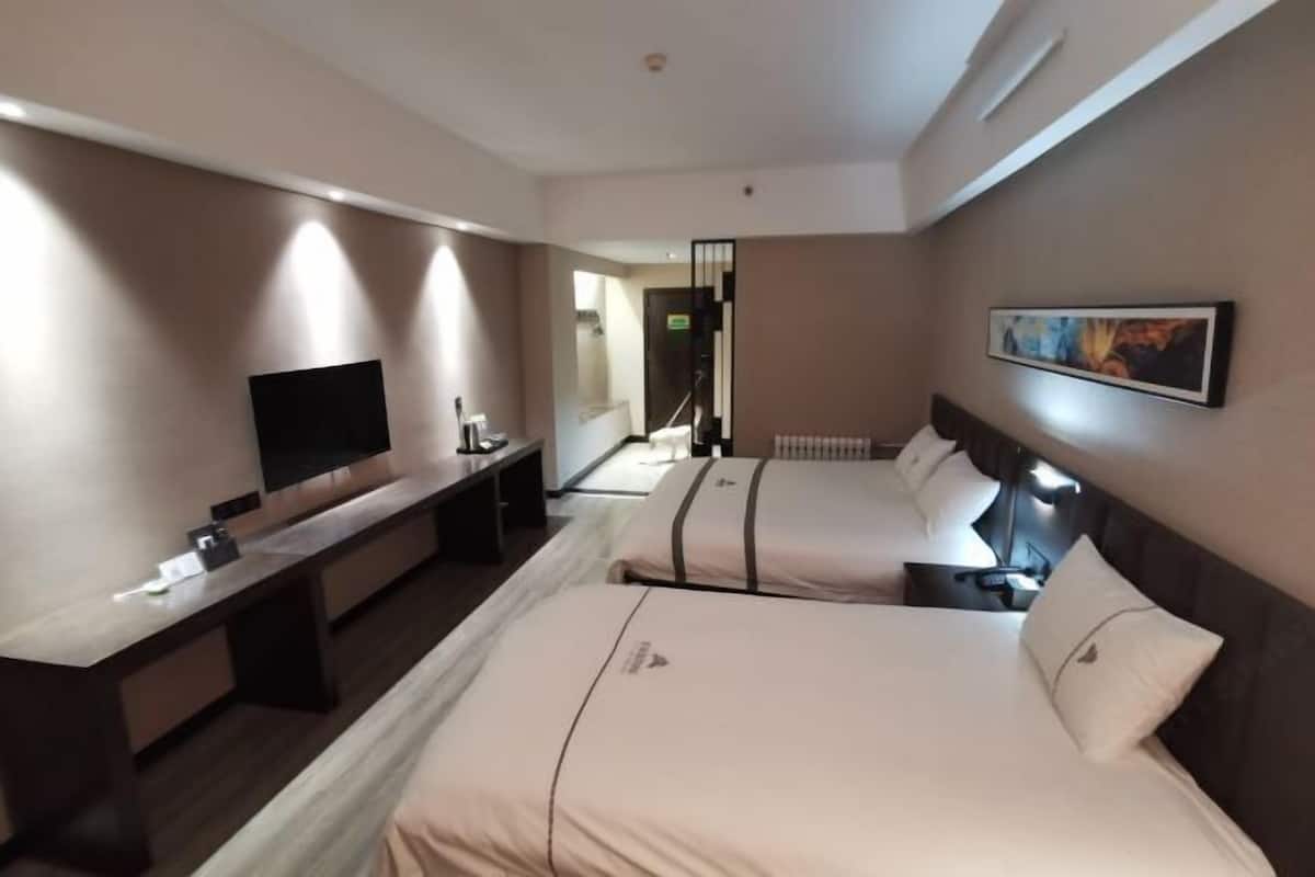 A hotel room with two beds, a desk, a flat-screen TV, a painting on the wall, and a window.
