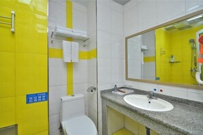 A bathroom with yellow and white tiles, a white toilet, a sink with a mirror, and a shower area.