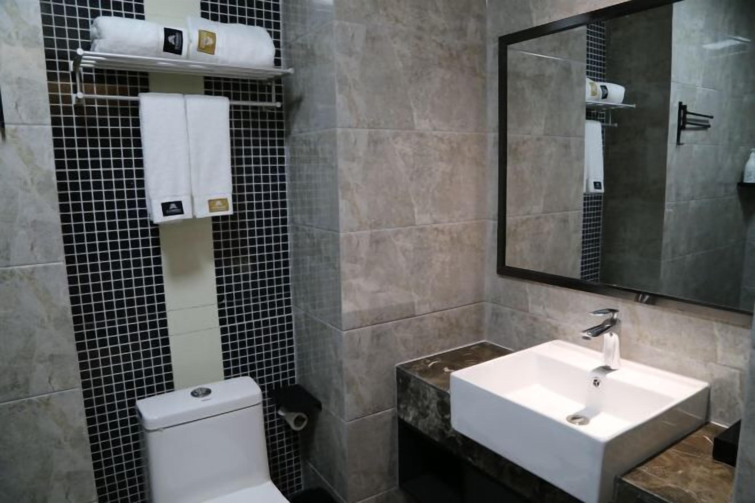 A bathroom with a toilet, a sink, and a mirror. There are towels on a shelf above the toilet.
