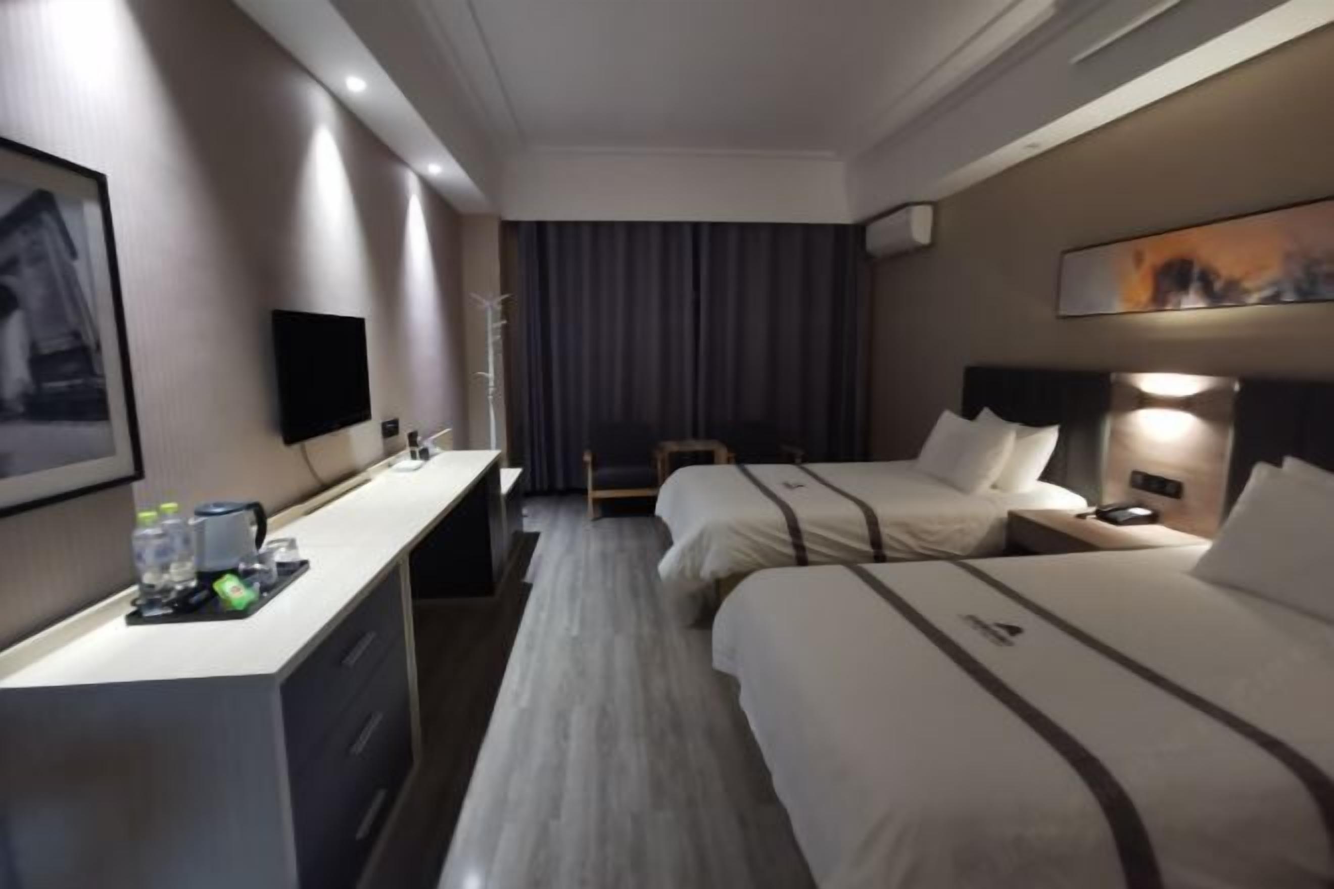 Et hotelværelse med to senge, et skrivebord med stol, et fjernsyn og et billede på væggen.