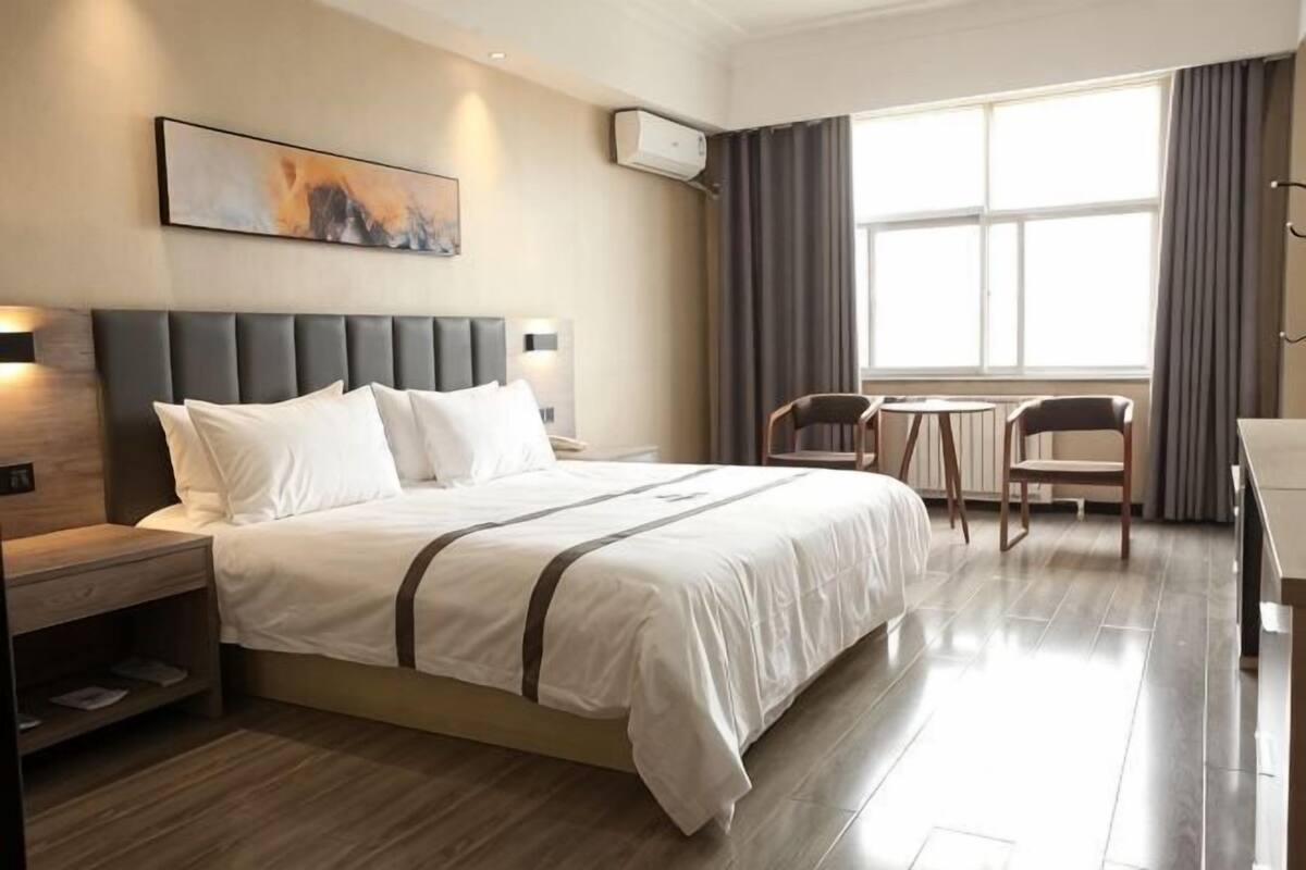 A hotel room with a bed, bedside tables, a desk, chairs, and a large window.