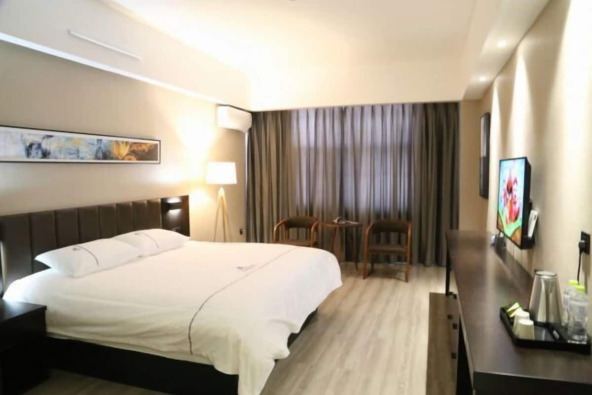 A hotel room with a bed, a desk, a chair, a TV, and a painting on the wall.