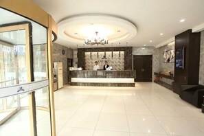 A hotel lobby with a reception desk, a chandelier, and a large window.