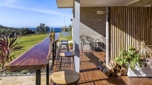 A wooden deck with a long table and chairs, a bamboo screen, and a view of the ocean.