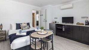 A modern bedroom with a bed, bedside tables, a small round table with chairs, a TV, and a kitchenette.