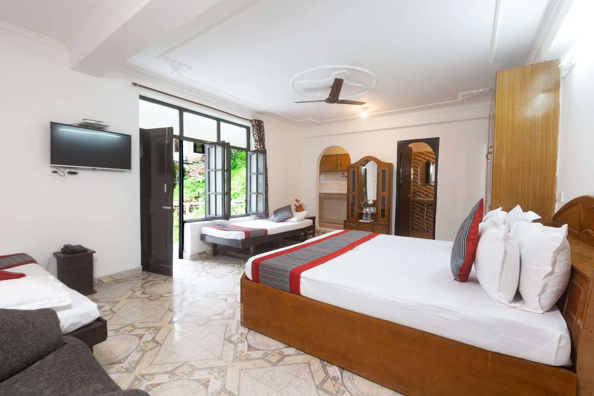 A hotel room with a large bed, a TV mounted on the wall, a wardrobe, and a bathroom visible through an open door.