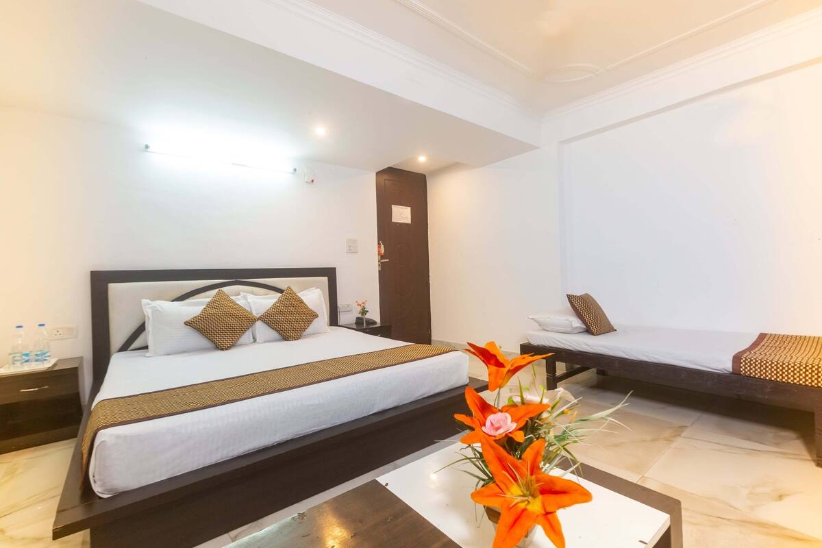 A hotel room with a large bed, a smaller bed, a nightstand with a lamp, and a vase with flowers on a table.