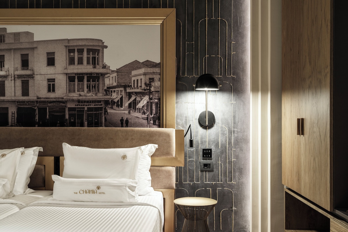 Una habitación de hotel con una cama grande, una lámpara de pared y un mural antiguo con un paisaje urbano.