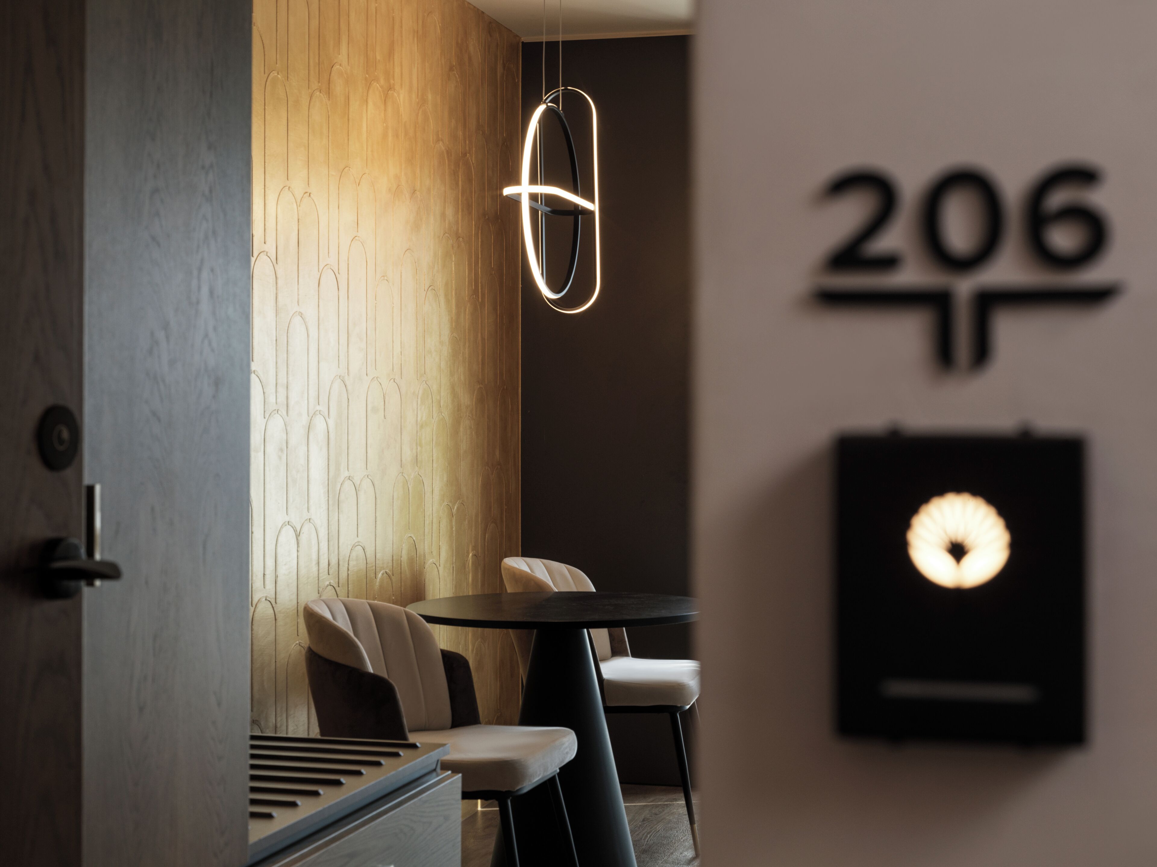 A modern interior with a wooden wall, a circular light fixture, and a wall-mounted sign displaying the number 206.