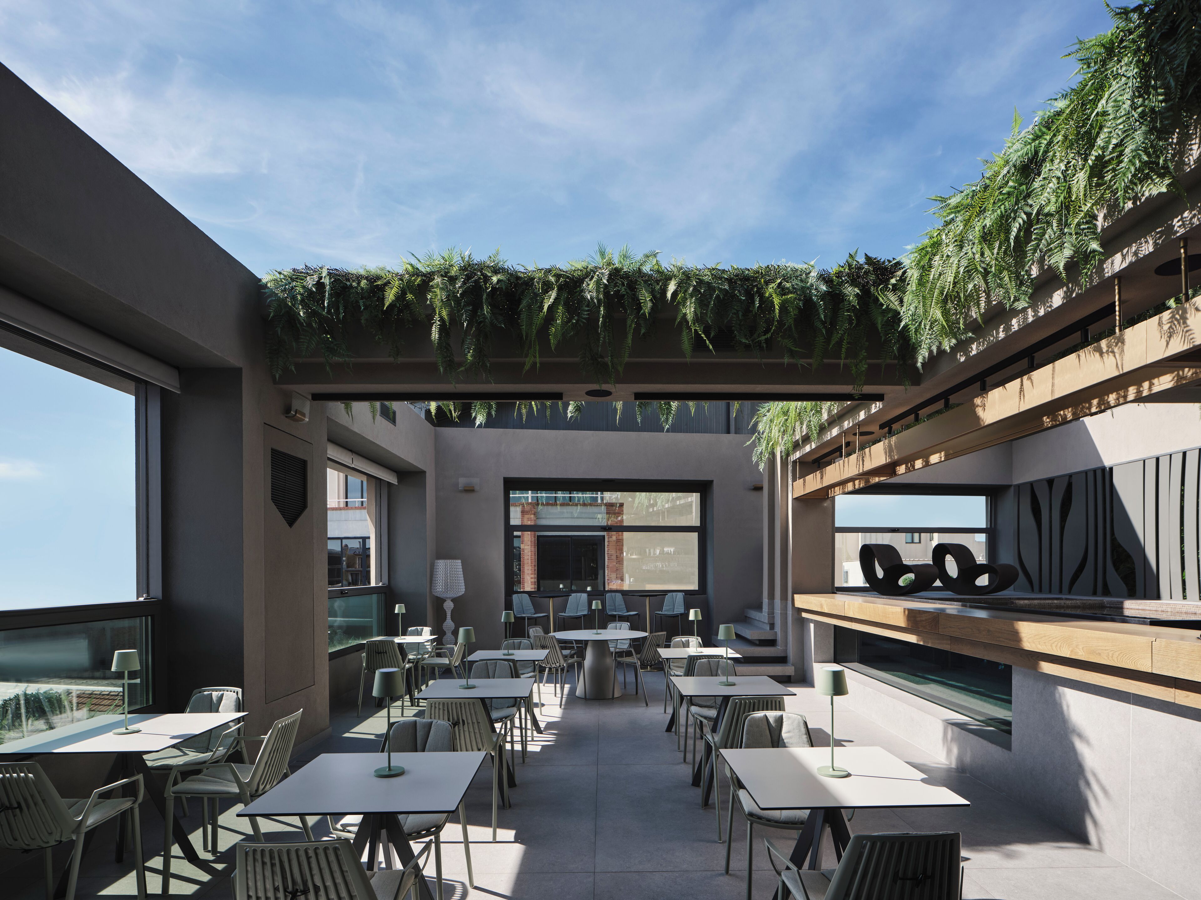 A rooftop dining area with tables and chairs, large windows, and a view of the city.
