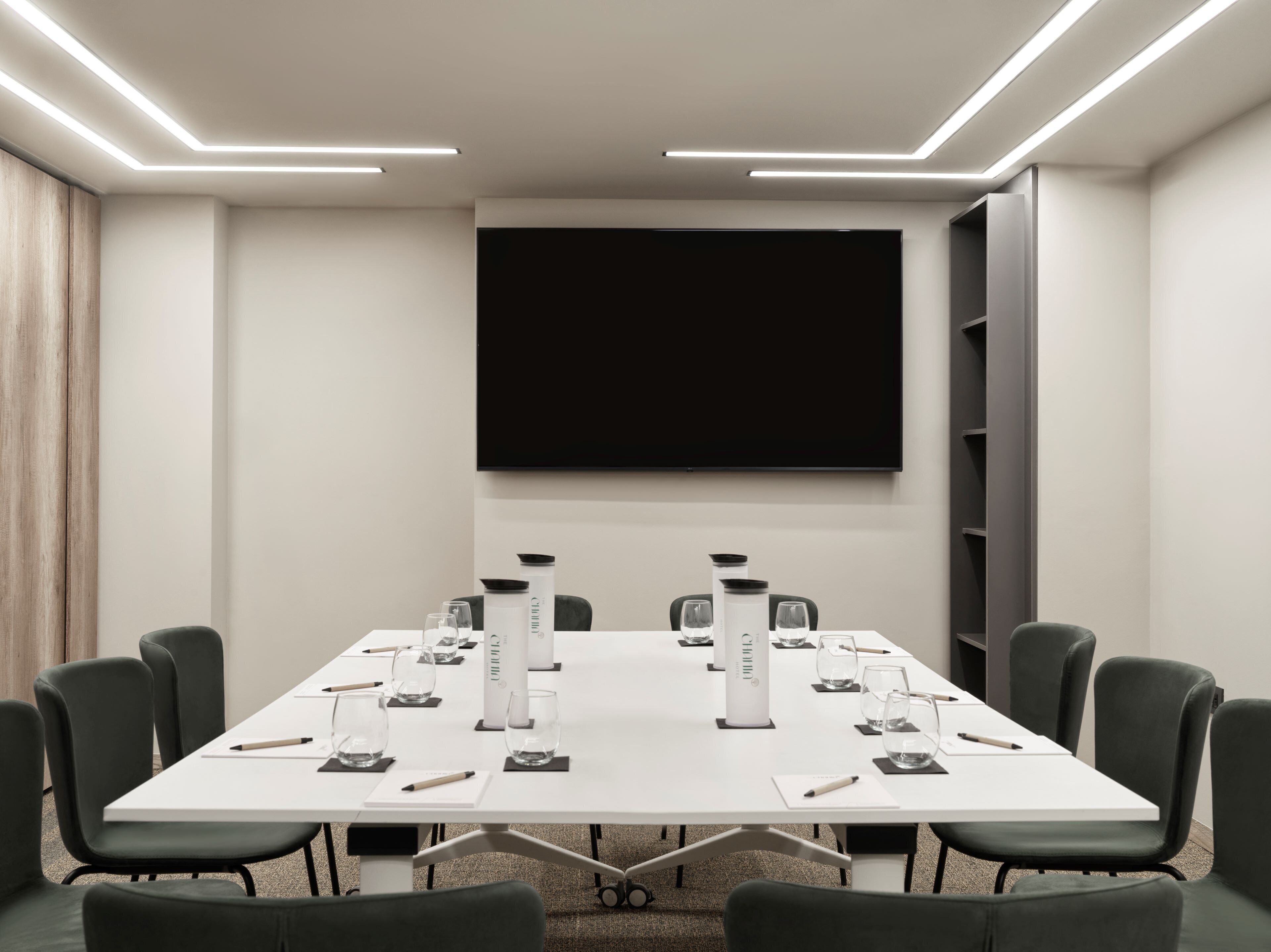 A conference room with a long table, chairs, a large screen, and water bottles.