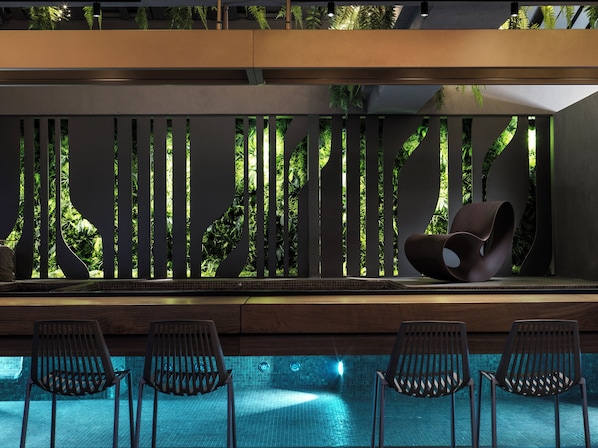 Un área de piscina moderna con un conjunto de sillones y una pared decorativa con listones verticales.