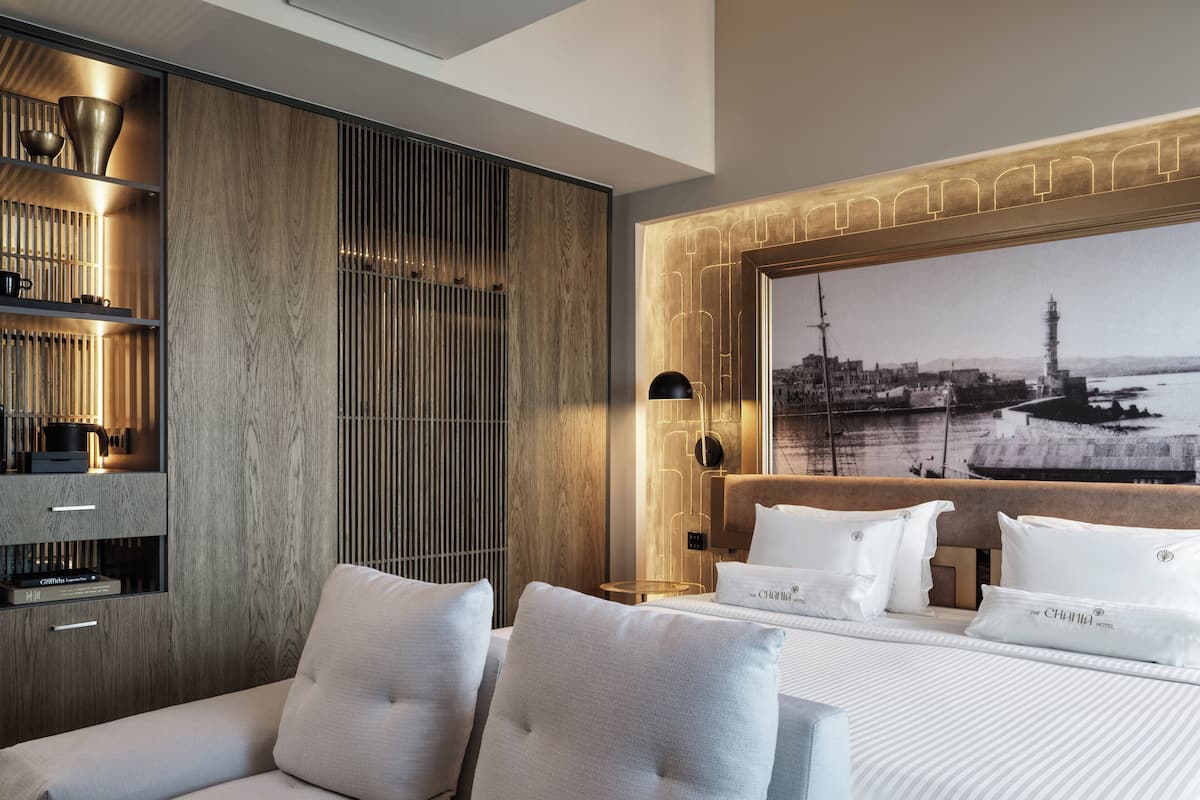 Une chambre d’hôtel moderne, équipée d’un lit, d’un canapé, d’un mur recouvert de panneaux en bois et d’un grand tableau encadré représentant un port.