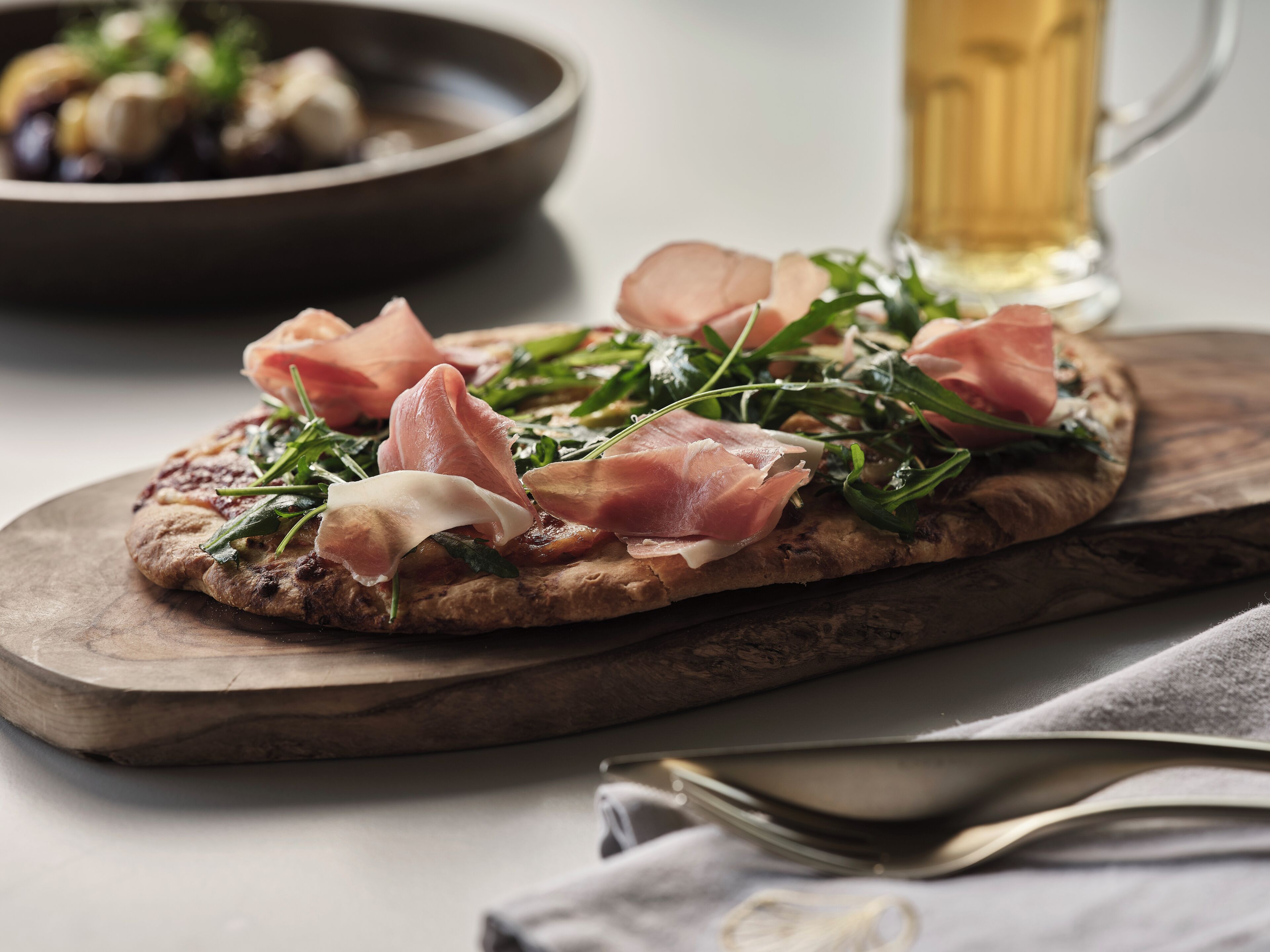A pizza on a wooden board with greens and prosciutto.