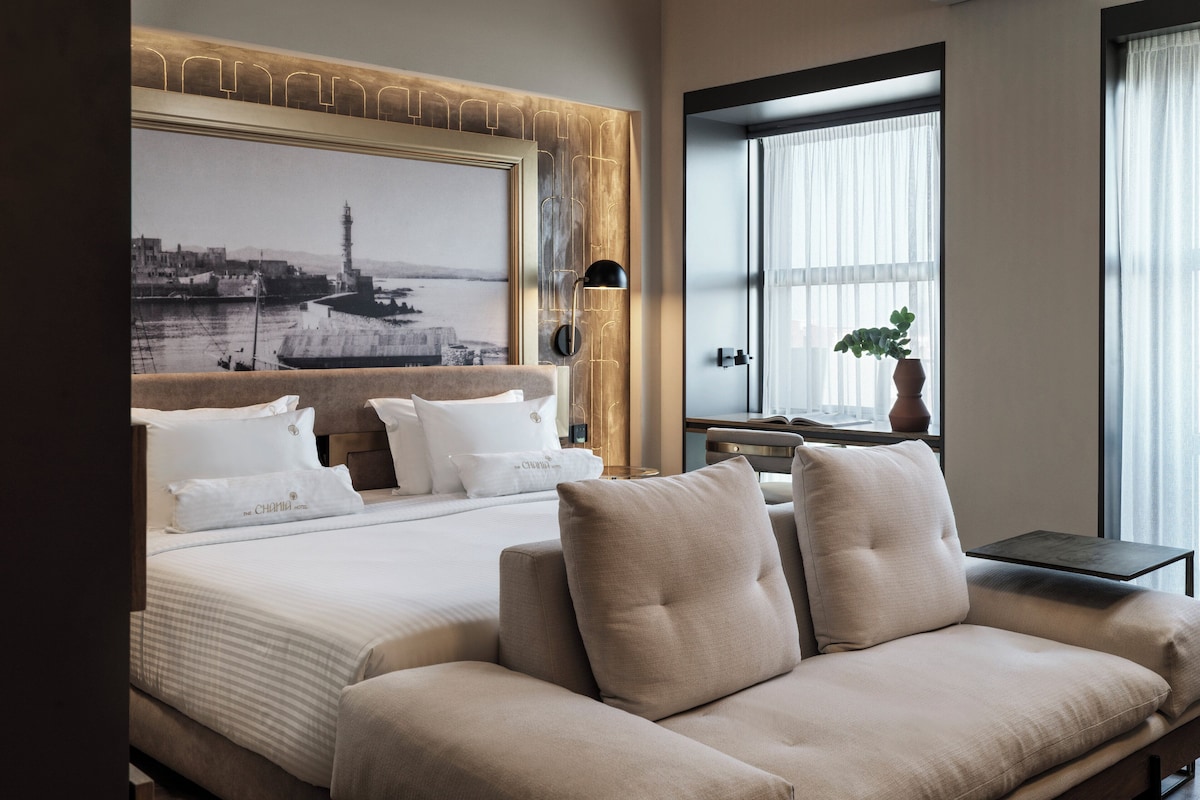 Una habitación de hotel moderna con una cama grande, un sofá, un escritorio y un ventanal con cortinas.