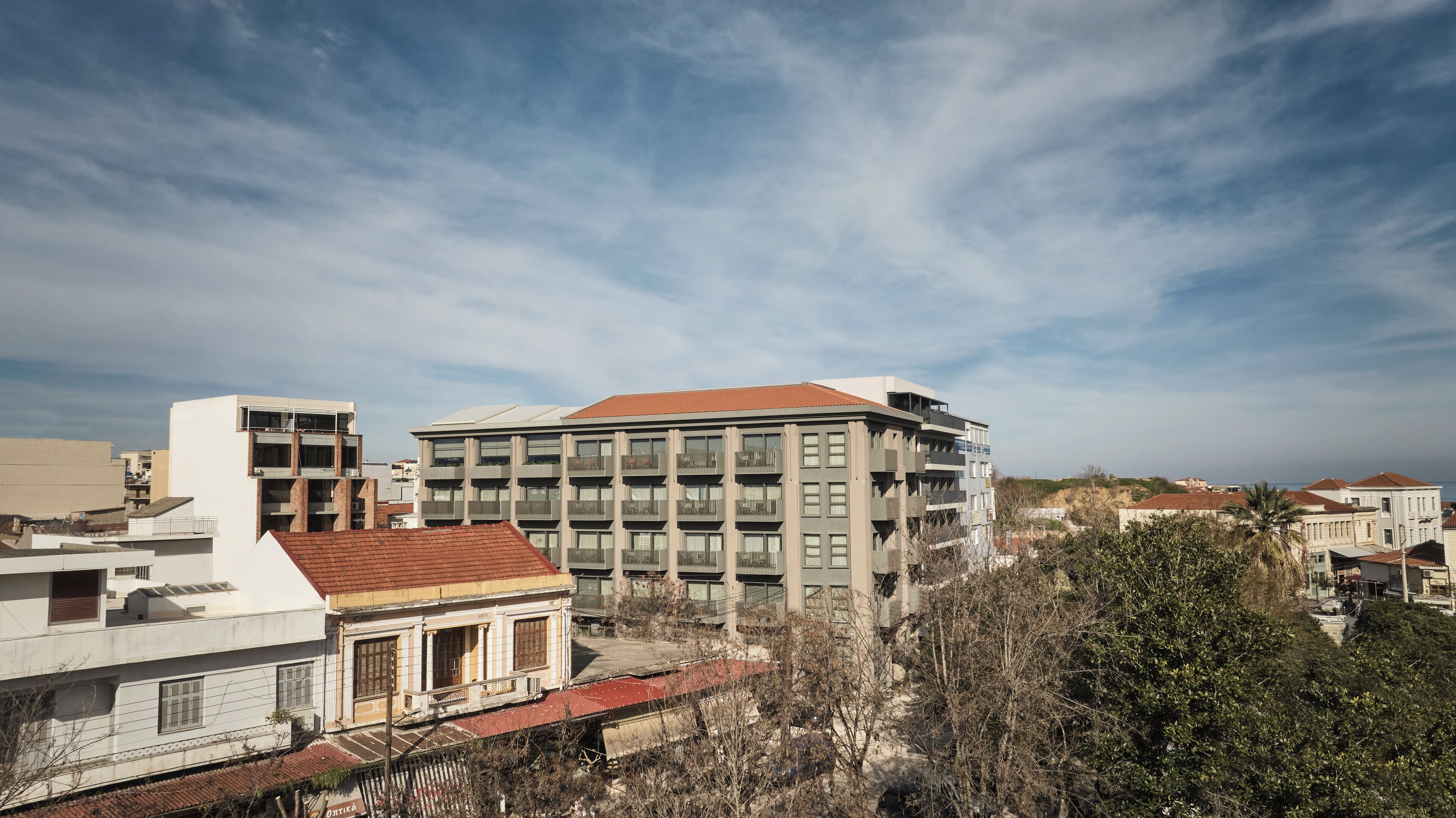 Edifici modern amb diversos balcons i un teulat vermell, envoltat d'altres edificis i arbres.