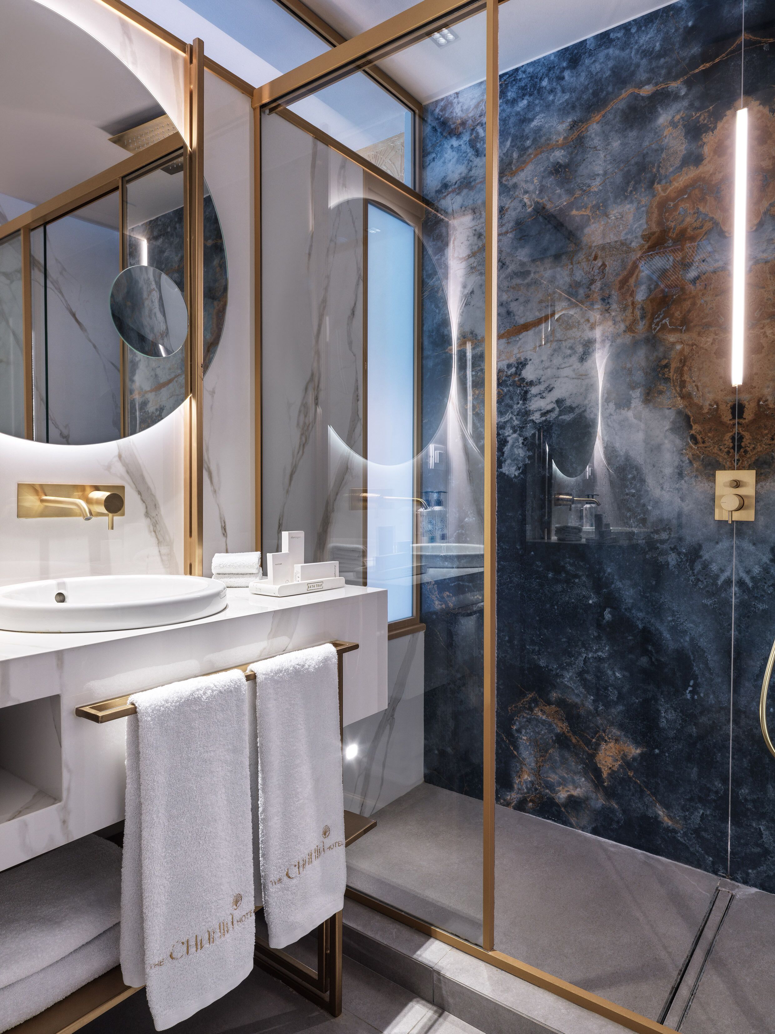 A modern bathroom with a marble vanity, a large mirror, and a glass-enclosed shower area.