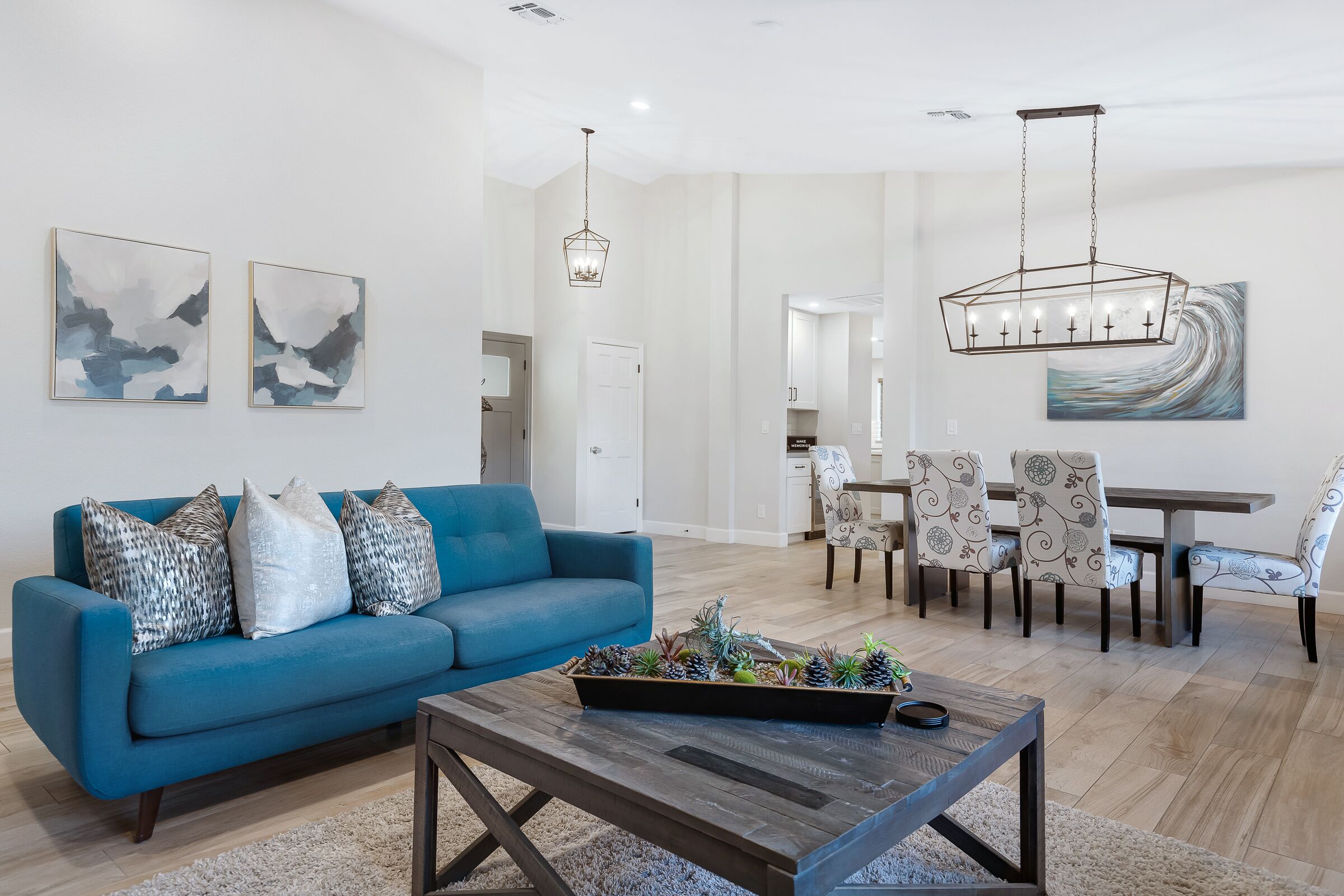 Una sala de estar moderna con un sofá azul, una mesa de centro con objetos decorativos, un comedor con sillas estampadas y arte abstracto en la pared.