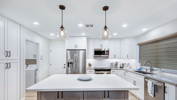 Una cocina moderna con armarios blancos, electrodomésticos de acero inoxidable y una isla central con taburetes.
