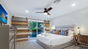 Un dormitorio moderno con una cama grande, un ventilador de techo y una puerta corrediza tipo granero que da a un balcón.