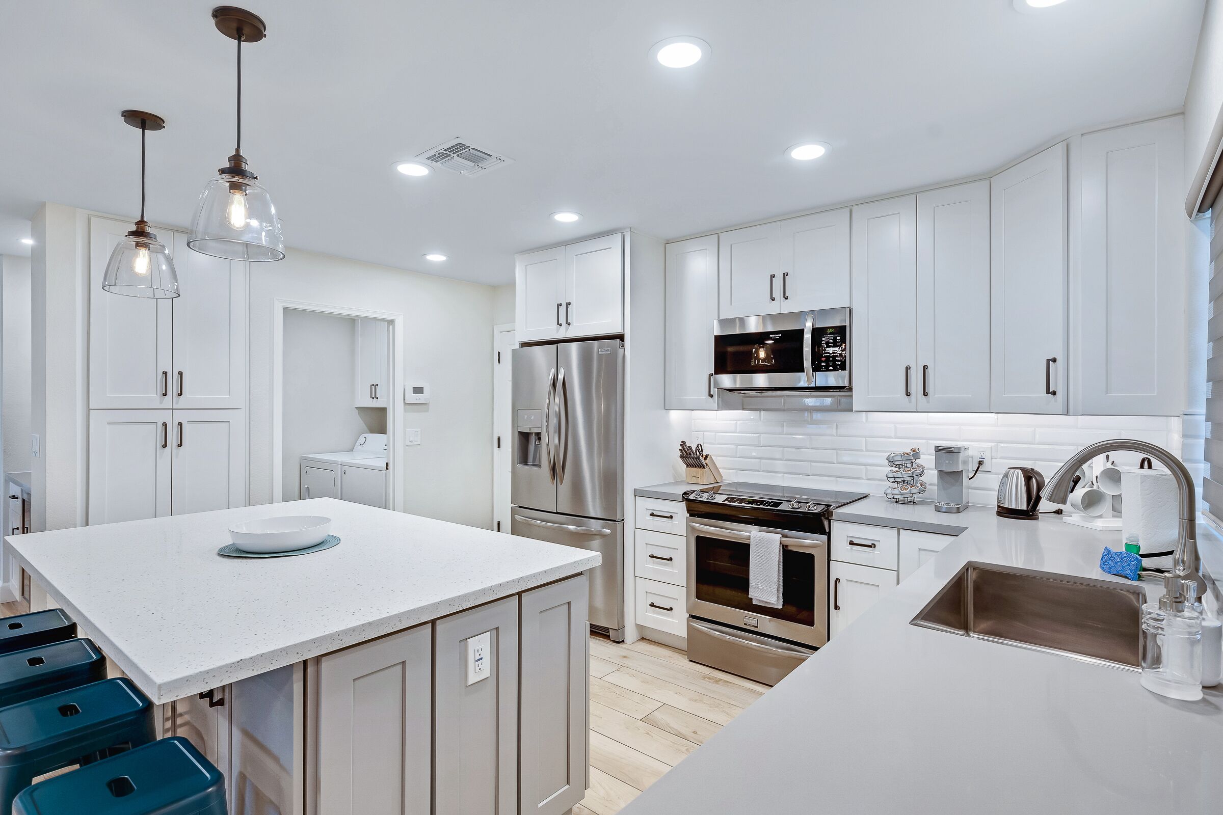 A modern kitchen with white cabinetry, stainless steel appliances, and pendant lighting.