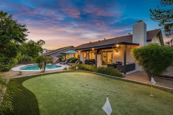 A backyard with a pool, a lawn, and a patio area with outdoor seating.