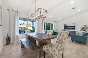 A dining area with a wooden table and benches, a sofa with patterned upholstery, and a hanging light fixture.