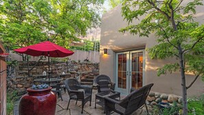 An outdoor patio with wicker furniture, a red umbrella, and a large red vase. - Casa La Vereda | Luxury Retreat Near Plaza (Santa Fe)