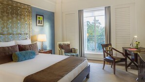 Habitación de hotel con una cama grande, dos mesitas de noche con lámparas, una silla, un escritorio y una ventana con vistas a zonas verdes.