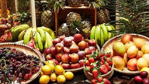 Diversas frutas expuestas en cestas y cajas, como manzanas, plátanos, uvas y naranjas.
