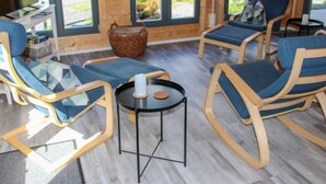 A modern interior with wooden walls, large windows, and a seating area with blue cushioned chairs and a glass table.