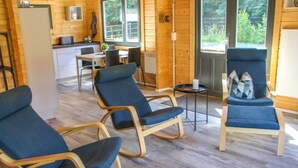 A cozy cabin interior with wooden walls, a dining area, and three blue lounge chairs.