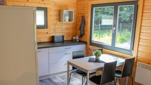 A compact kitchen with a dining table and chairs, a small refrigerator, and a window with a view of greenery.