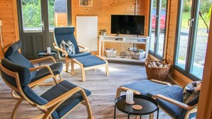 A cozy cabin interior with wooden walls, a TV, and seating areas with blue cushions.