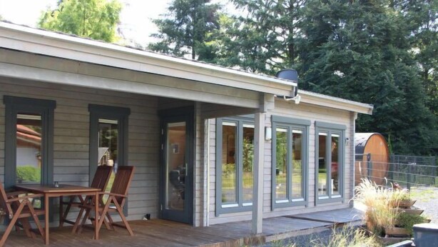 A wooden deck with a table and chairs, a covered patio area, and a view of the surrounding greenery.