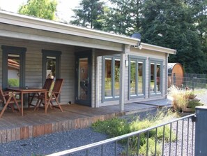 Une terrasse en bois avec une table et des chaises, un patio couvert et une vue sur la verdure environnante.