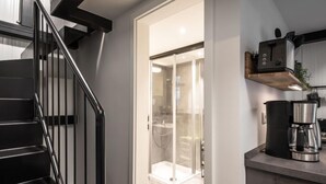 A modern kitchen with a coffee maker, a glass shower enclosure, and a staircase.