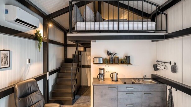 A modern loft-style room with a mezzanine bed, a kitchen area with a sink and countertop, and a leather chair.